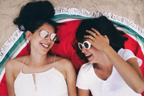 zwei frauen lachen und liegen auf einem strandtuch